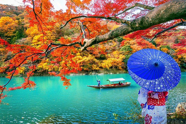 Traditionally dressed woman along the river in Kyoto with fall colors